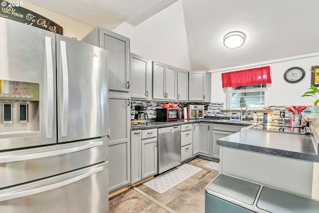 kitchen with a sink, appliances with stainless steel finishes, backsplash, gray cabinets, and dark countertops