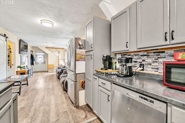 kitchen featuring tasteful backsplash, dark countertops, light wood-style flooring, a barn door, and appliances with stainless steel finishes