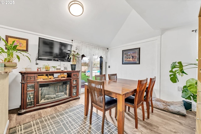 dining area featuring lofted ceiling, a glass covered fireplace, and wood finished floors