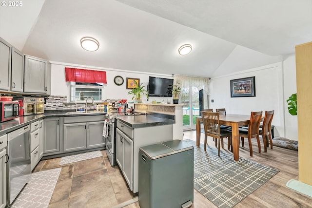 kitchen with stainless steel appliances, gray cabinetry, vaulted ceiling, a sink, and a peninsula