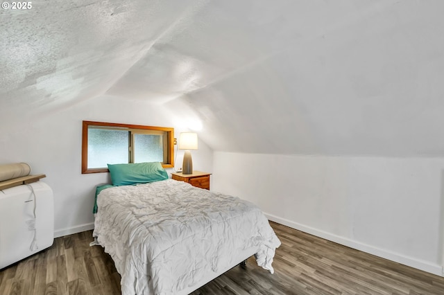 bedroom with a textured ceiling, baseboards, vaulted ceiling, and wood finished floors