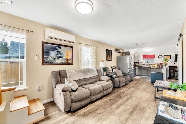 living area featuring a wall unit AC, light wood finished floors, a barn door, a textured ceiling, and baseboards