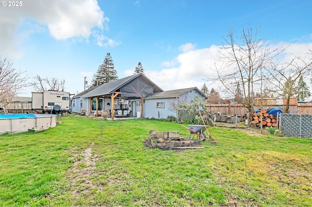 rear view of property with a fenced in pool, an outdoor fire pit, a fenced backyard, and a yard