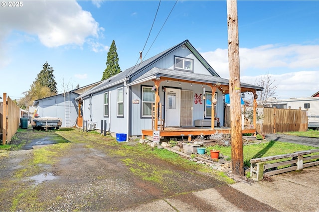 view of front of house featuring driveway, covered porch, and fence