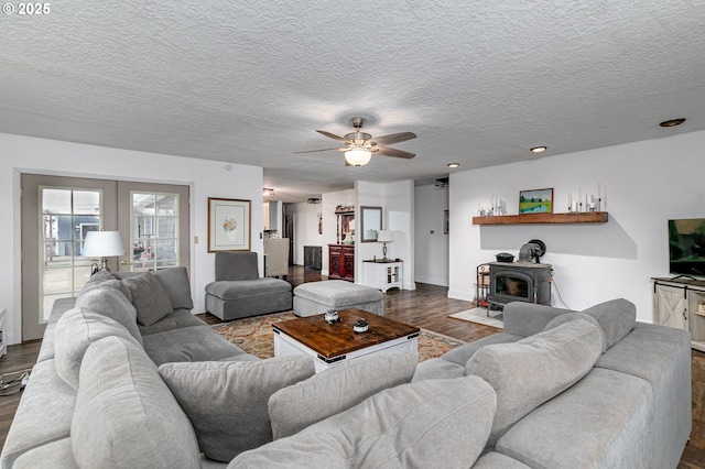 living room with french doors, dark wood-style flooring, a ceiling fan, a wood stove, and a textured ceiling