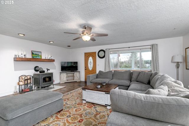 living area with a wood stove, ceiling fan, baseboards, and wood finished floors