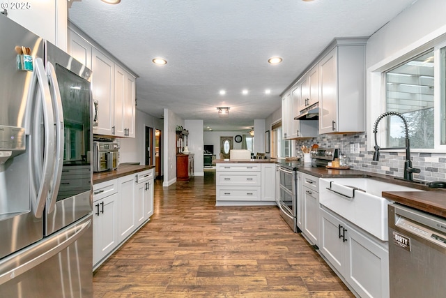 kitchen with wood counters, appliances with stainless steel finishes, dark wood-type flooring, a peninsula, and backsplash