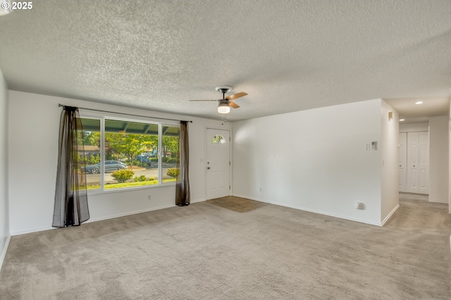 carpeted spare room featuring a textured ceiling, a ceiling fan, and baseboards