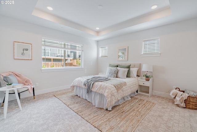 bedroom featuring recessed lighting, a tray ceiling, baseboards, and light carpet