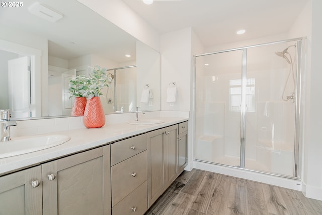 bathroom featuring a stall shower, wood finished floors, double vanity, and a sink