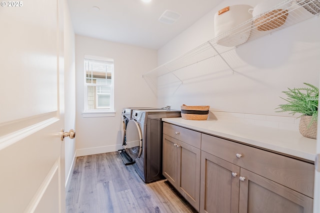 washroom featuring washing machine and dryer, cabinet space, baseboards, and light wood-style floors