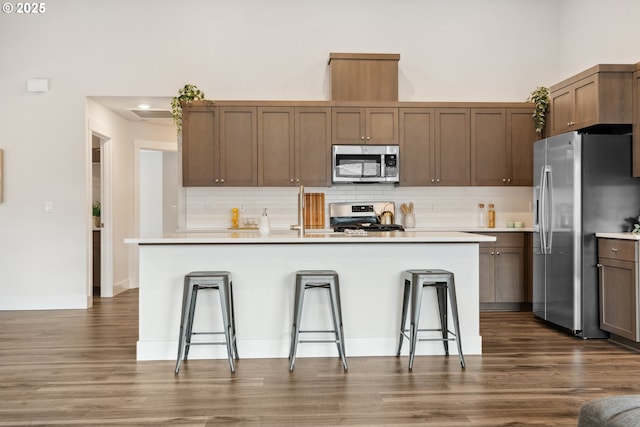 kitchen with stainless steel appliances, a kitchen bar, dark wood-type flooring, tasteful backsplash, and light countertops