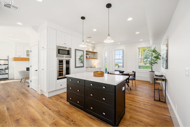 kitchen with white cabinets, wine cooler, light wood-style flooring, stainless steel microwave, and visible vents