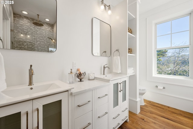 bathroom with a tile shower, wood finished floors, a sink, and double vanity