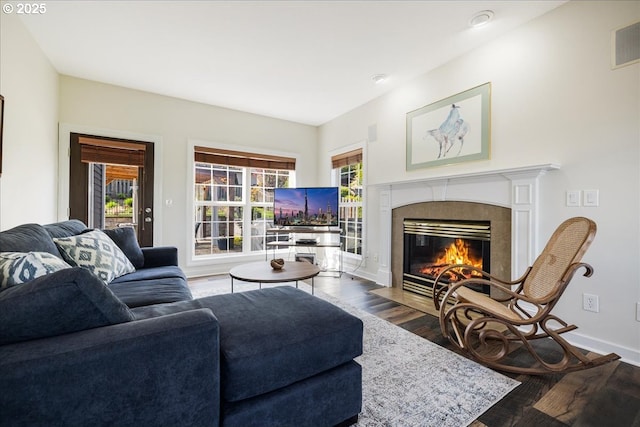 living area featuring a tiled fireplace, baseboards, wood finished floors, and visible vents