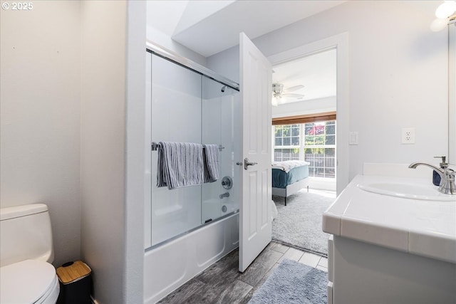 ensuite bathroom featuring vanity, wood finished floors, toilet, ceiling fan, and bath / shower combo with glass door