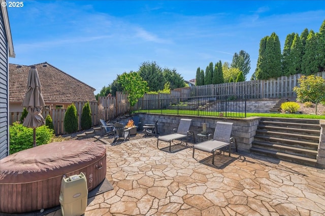 view of patio / terrace featuring a fenced backyard, a hot tub, and an outdoor fire pit