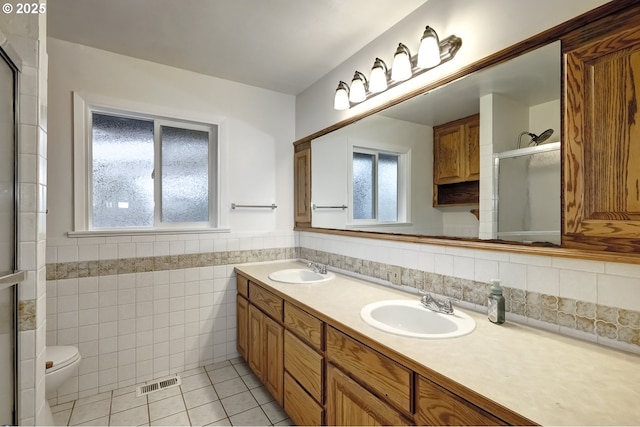 full bath with tile walls, visible vents, a sink, and a shower with shower door