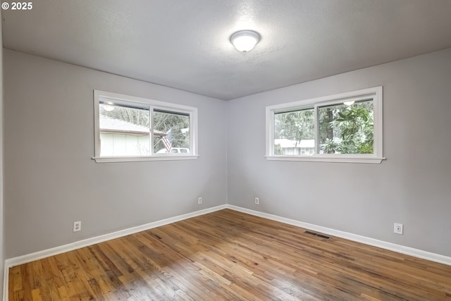 empty room featuring a textured ceiling, wood finished floors, visible vents, and baseboards