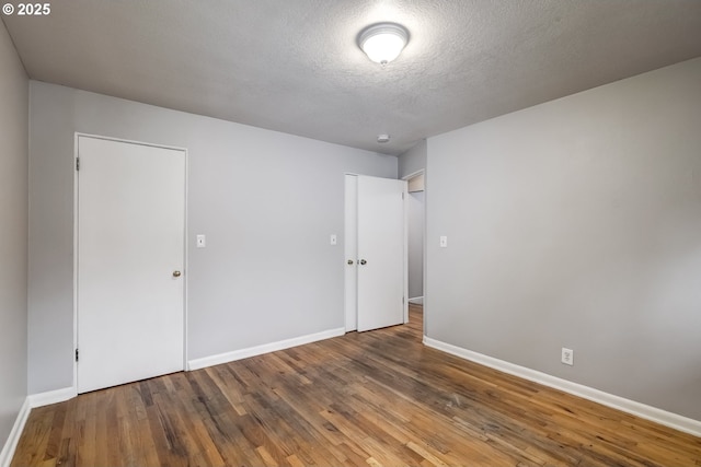 unfurnished room with wood-type flooring, a textured ceiling, and baseboards