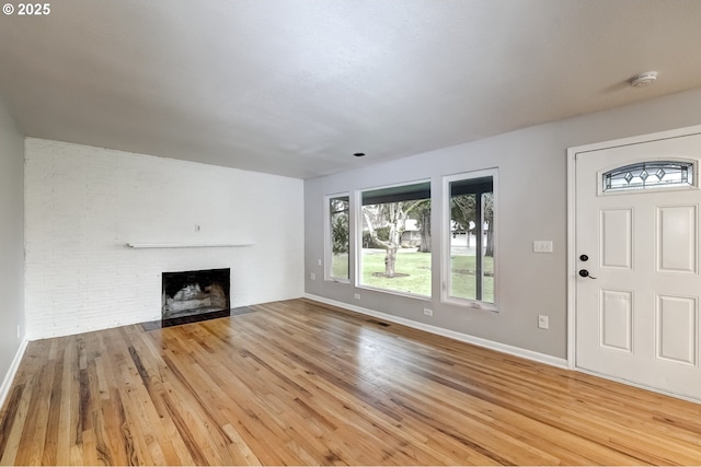 unfurnished living room featuring a brick fireplace, light wood-style flooring, and baseboards