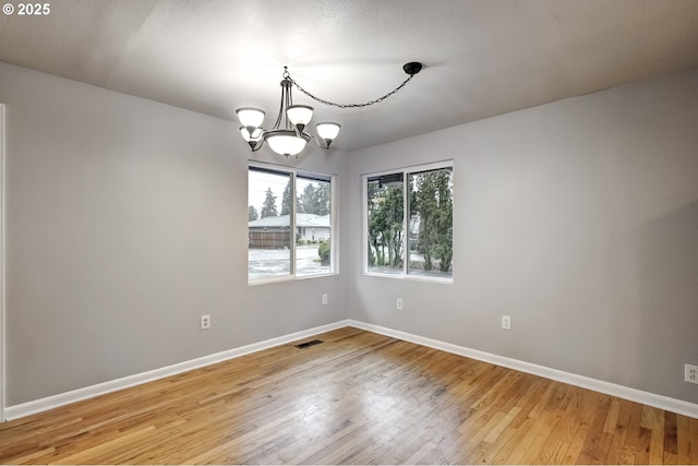 unfurnished room featuring light wood-type flooring, visible vents, baseboards, and an inviting chandelier