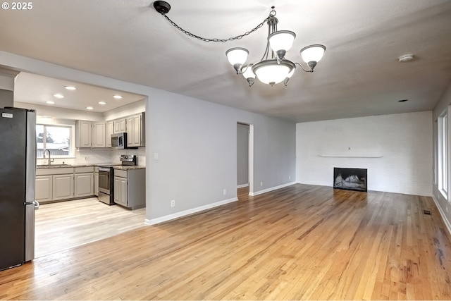 unfurnished living room with a chandelier, a large fireplace, a sink, baseboards, and light wood-style floors