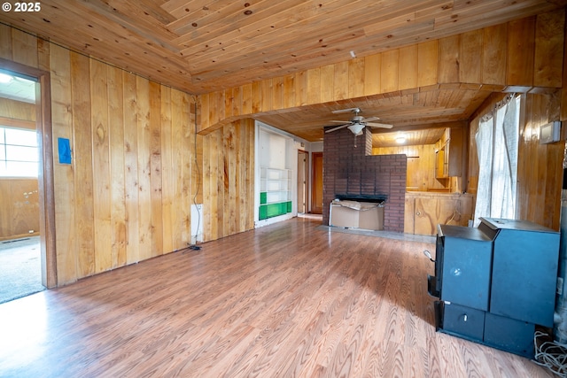 unfurnished living room featuring wooden walls, wooden ceiling, a fireplace, wood finished floors, and a ceiling fan