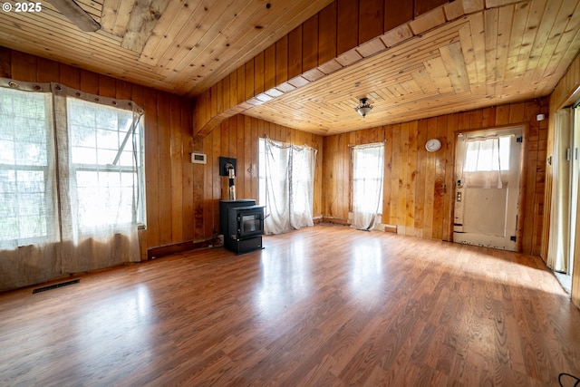 unfurnished living room featuring wood finished floors, a wood stove, plenty of natural light, and wood ceiling