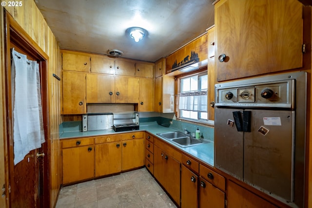 kitchen with brown cabinetry, visible vents, a sink, light countertops, and wall oven