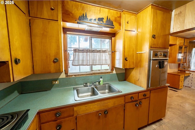 kitchen featuring cooktop, light countertops, brown cabinets, and a sink