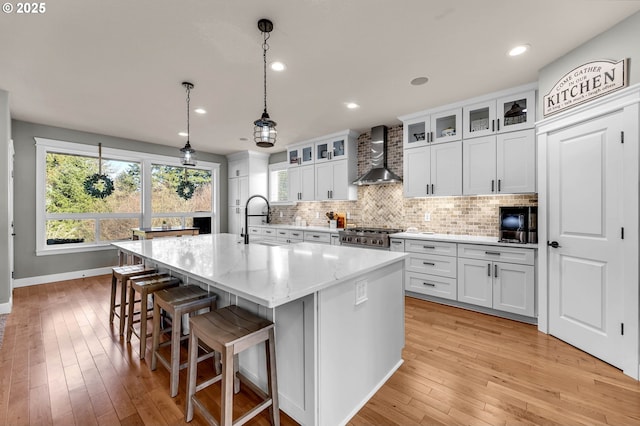 kitchen featuring tasteful backsplash, stove, light wood-style floors, a kitchen island with sink, and wall chimney exhaust hood