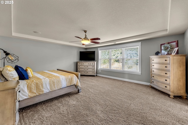 bedroom with a textured ceiling, ceiling fan, baseboards, a tray ceiling, and carpet