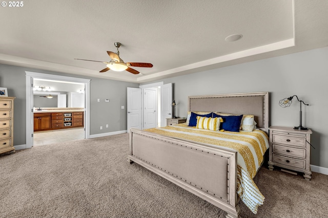 carpeted bedroom with a ceiling fan, a raised ceiling, connected bathroom, and baseboards