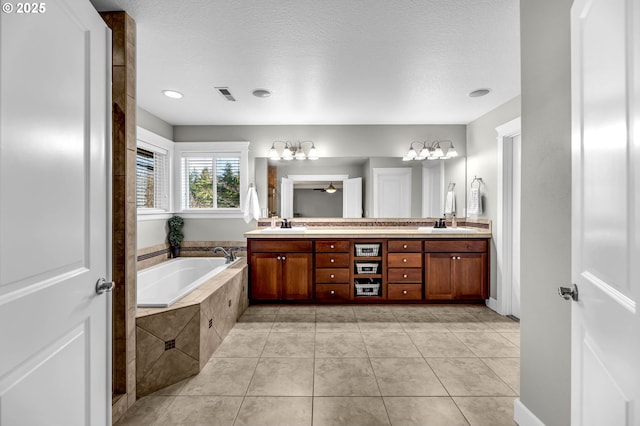 bathroom with a textured ceiling, tile patterned flooring, visible vents, a bath, and double vanity