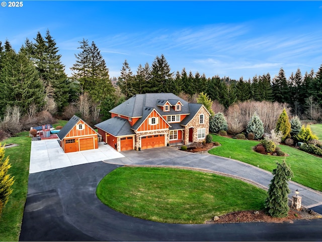 view of front of house featuring driveway, board and batten siding, stone siding, a front lawn, and a wooded view