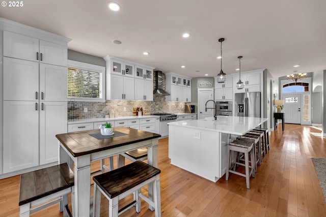 kitchen with backsplash, light wood-style flooring, appliances with stainless steel finishes, white cabinetry, and wall chimney range hood