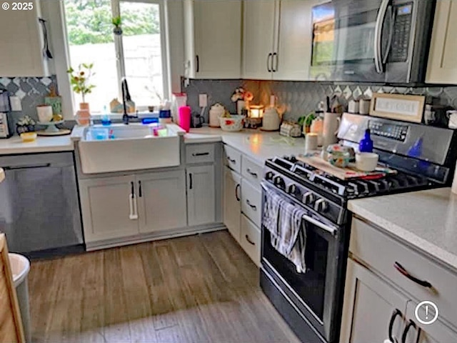 kitchen with sink, backsplash, appliances with stainless steel finishes, white cabinets, and light wood-type flooring