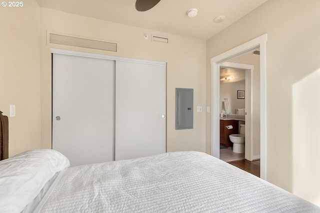 bedroom featuring ensuite bathroom, dark wood-type flooring, electric panel, and a closet