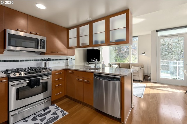 kitchen with sink, light hardwood / wood-style flooring, stainless steel appliances, decorative backsplash, and kitchen peninsula