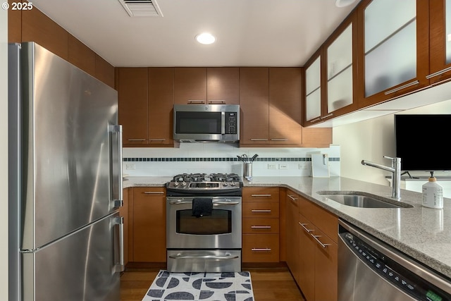 kitchen featuring dark hardwood / wood-style floors, sink, decorative backsplash, stainless steel appliances, and light stone countertops