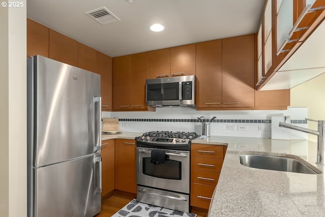 kitchen featuring light stone counters, stainless steel appliances, sink, and backsplash