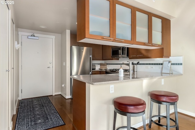 kitchen featuring appliances with stainless steel finishes, dark wood-type flooring, a kitchen breakfast bar, and kitchen peninsula