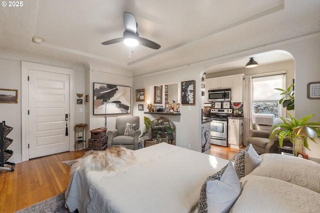 bedroom with ceiling fan, a raised ceiling, and light wood-type flooring