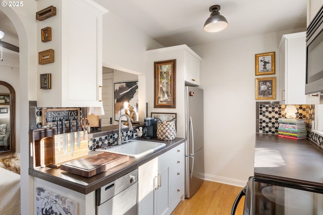 kitchen with sink, white cabinets, decorative backsplash, stainless steel appliances, and light wood-type flooring