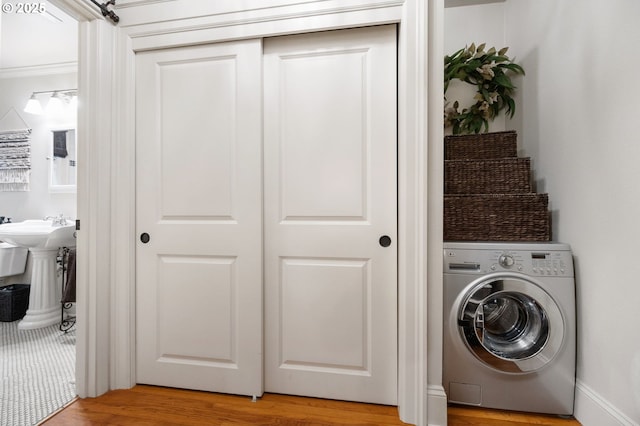 clothes washing area with ornamental molding, washer / dryer, sink, and light wood-type flooring