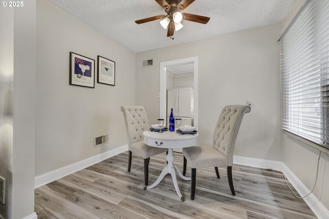 dining area with a ceiling fan, a textured ceiling, light wood finished floors, and baseboards