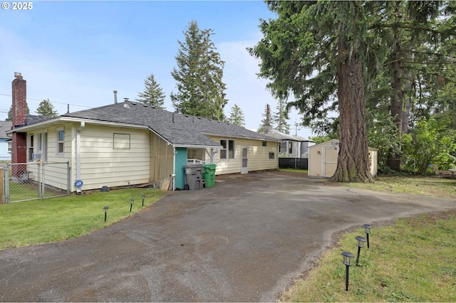view of front of home with a storage unit, an outdoor structure, asphalt driveway, a chimney, and a shingled roof