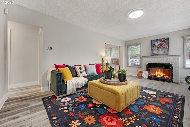 living room with a textured ceiling, wood finished floors, a lit fireplace, and baseboards