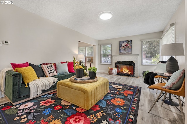living room with a textured ceiling, a glass covered fireplace, wood finished floors, and baseboards